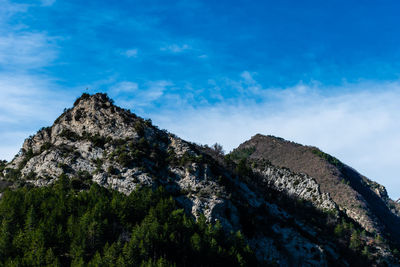 Low angle view of rocks on mountain against blue sky