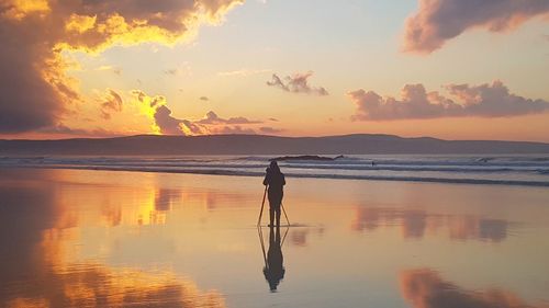 Silhouette man standing on beach against sky during sunset