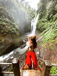 Fashionable woman standing by waterfall amidst mountains