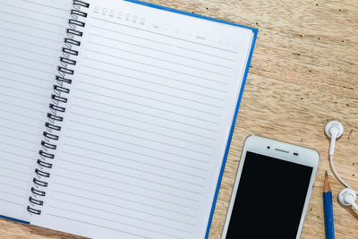 Directly above shot of blank open book with pencil and mobile phone on wooden table