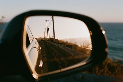 Reflection of road in side-view mirror against sky at sunset