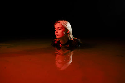 Female blonde swims at night under red lighting