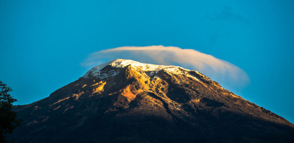 Low angle view of snowcapped mountain against blue sky