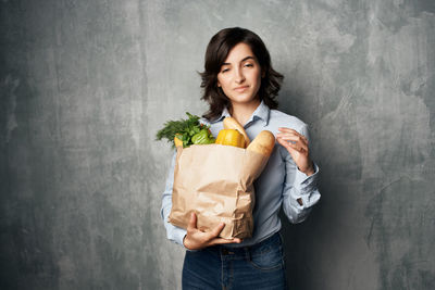 Portrait of young woman holding ice cream standing against wall