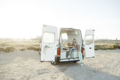 Young freelancer sitting with laptop in caravan in front of clear sky