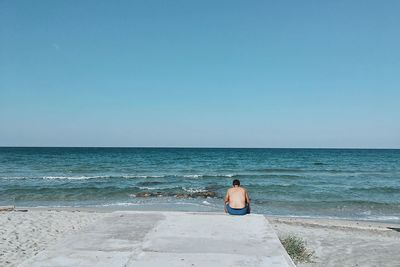 Rear view of man on beach against clear sky