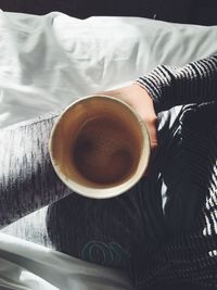 Close-up of hand holding coffee cup on bed