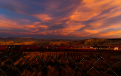 Fence on field against sky during sunset