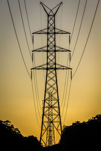 Low angle view of silhouette electricity pylon against sky at sunset