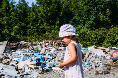 Little girl at a dump among a heap of scattered garbage in the forest.