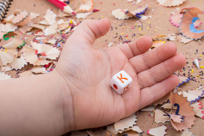 Cropped hand of child holding dice on messy table
