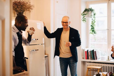 Smiling friends drinking water while standing by refrigerator in kitchen