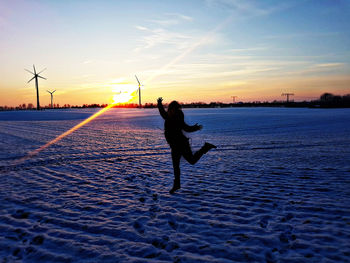 Silhouette woman on snow covered land against sky during sunset