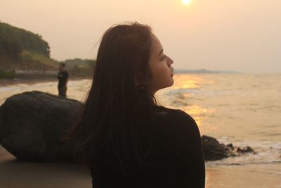 Woman standing at beach against sky during sunset