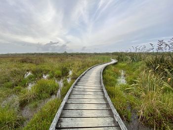 Dirt road amidst plants on field against sky