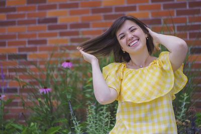 Portrait of a smiling young woman standing against yellow wall