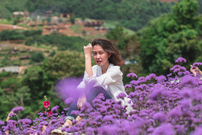 Portrait of beautiful woman sitting by purple flowering plants