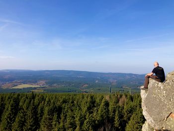 Rear view of man sitting on mountain against sky