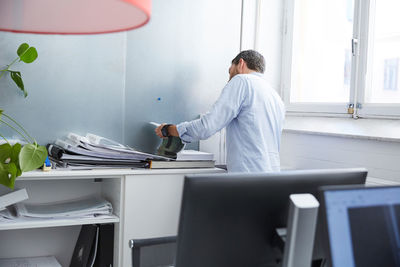 Businessman reading book while standing by window in creative office