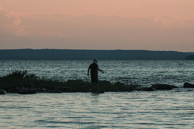 Silhouette man standing in sea against sky during sunset