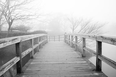 Empty wooden footbridge in winter during foggy weather