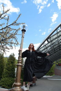 Full length of woman in oversized black dress walking to nowhere against built structure outdoors