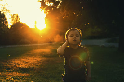 Portrait of boy standing on grassy field in backyard during sunset