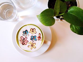 Directly above view of floral pattern froth art in latte by houseplant on table at cafe