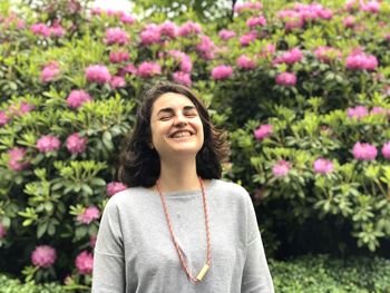 Smiling young woman standing against pink flowering plants