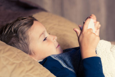 Boy using digital tablet while lying on bed at home