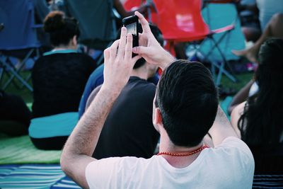 Rear view of man photographing from mobile phone at park