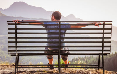 Rear view of mature man sitting on bench against mountain