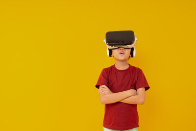 Boy wearing vr box standing against yellow background