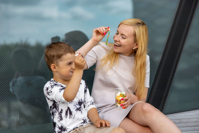 Happy blond woman and little boy sitting on terrace and eating sweets. mother and son enjoy