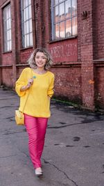 Portrait of smiling young woman walking on street by building in city