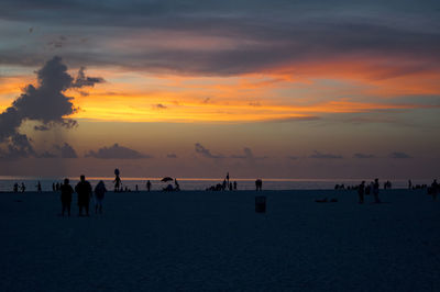 People at beach against sky during sunset