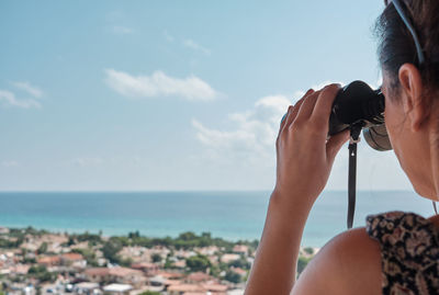 Midsection of woman photographing sea against sky