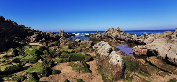 Panoramic view of rocks and sea against clear blue sky