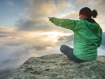 Rear view of man sitting on rock against sky