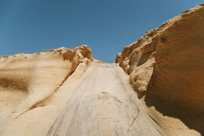 Low angle view of road amidst rock formations against clear blue sky