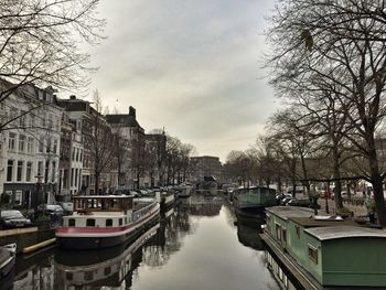Boats moored on canal in city against sky