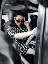 A girl wearing a polkadot dress, sun glasses and high boots sitting in a car 