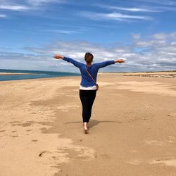 Full length of woman with arms raised on beach against sky