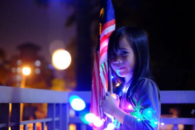 Portrait of smiling girl holding flag at night 