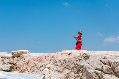 Woman standing on rock against blue sky