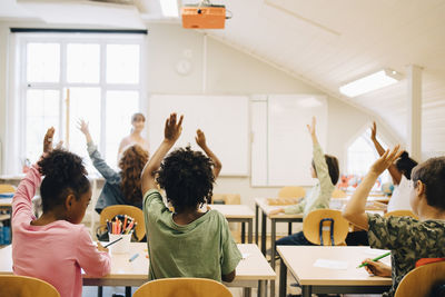 Students raising hands while answering in classroom at school