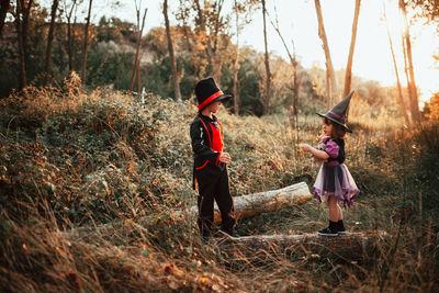 Girl wearing witch hat standing with brother at forest during halloween