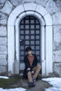 Portrait of young man sitting by door during winter