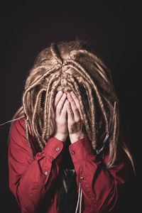 Close-up of mid adult man with blond hair hiding face while standing against black background