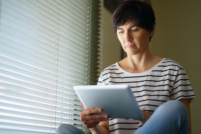 Woman using digital tablet while sitting by window